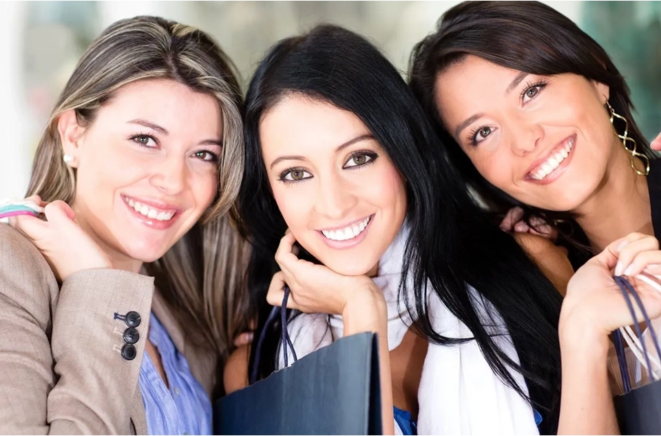 Three women smiling for the camera with a bag.