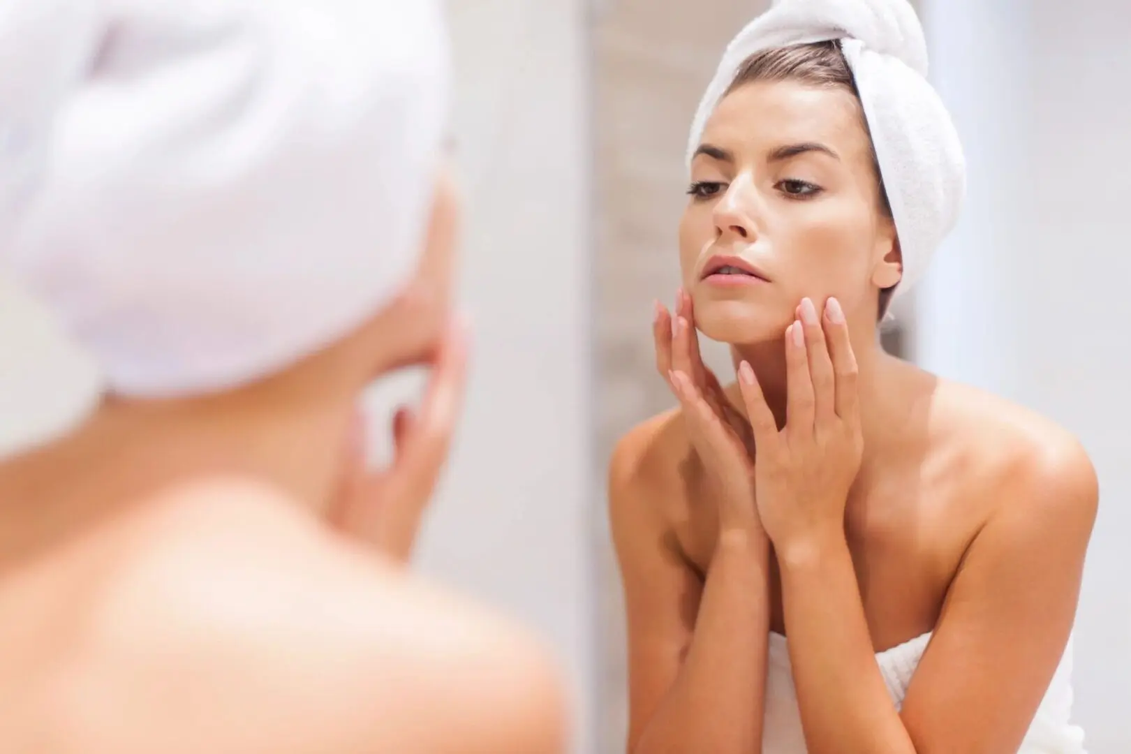 A woman with her hands on her face looking in the mirror.