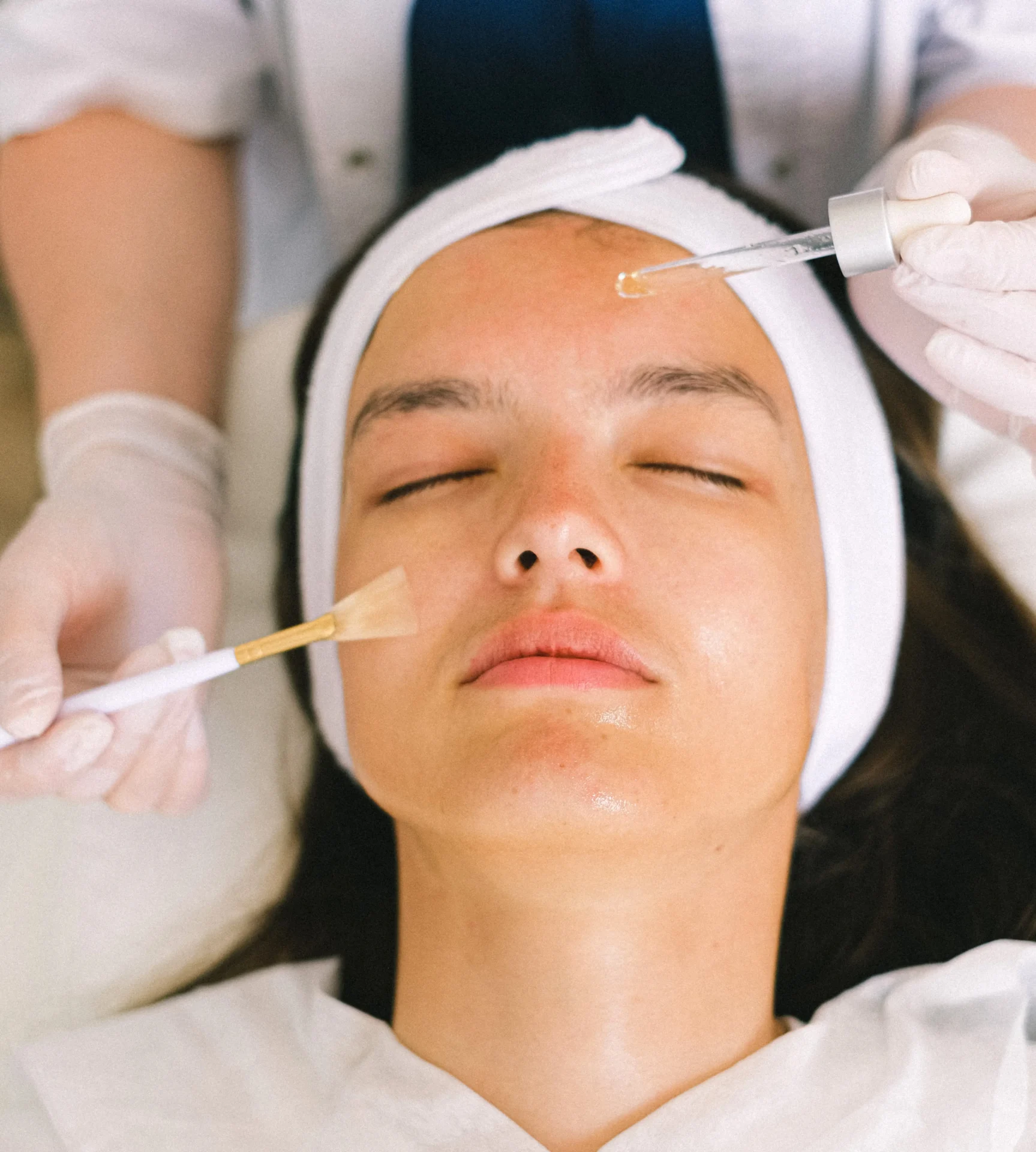 A woman getting her face waxed by two estheticians.